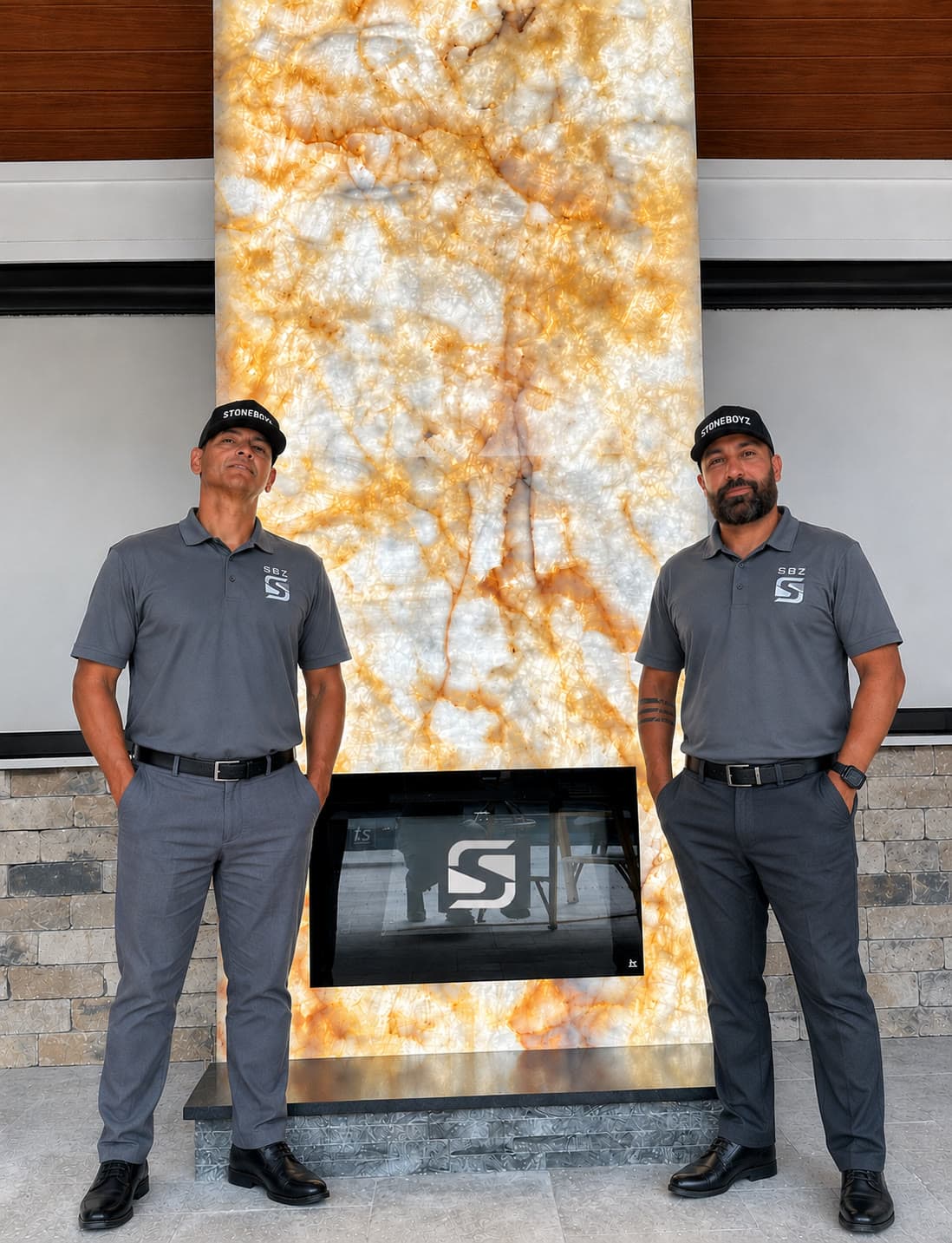 The two Stone Boyz owners in front of a backlit onyx fireplace wall they built